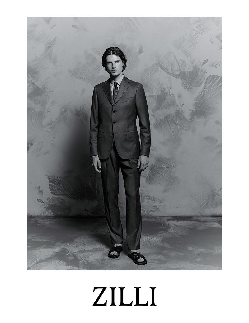 Monochrome full shot of a male fashion model wearing a suit with dress shoes against a textured backdrop, advertising Zilli.