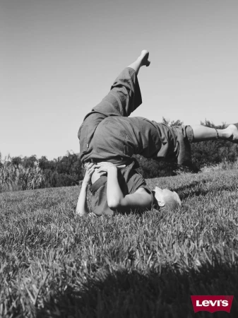 Monochrome shot of an adult doing a headstand in a grassy field with trees in the background, set against a clear sky.
