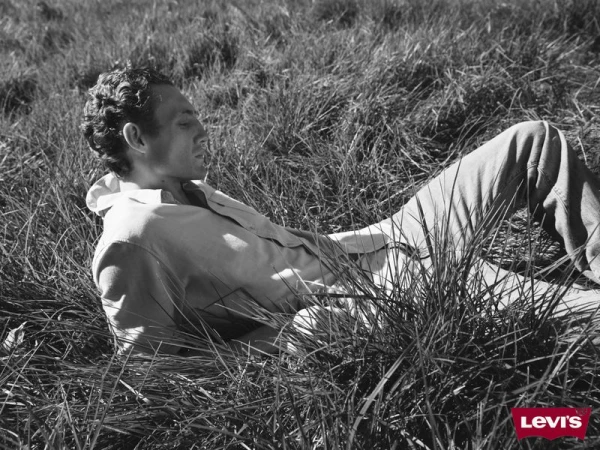 Black and white image of a man lying in the grass wearing a shirt, capturing a peaceful outdoor moment with a Levi's logo in the corner.