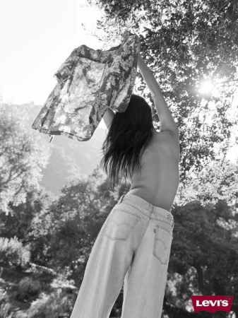 Monochrome shot of a woman wearing jeans, holding up a floral shirt against a backdrop of trees and sunlight with the Levi's logo.