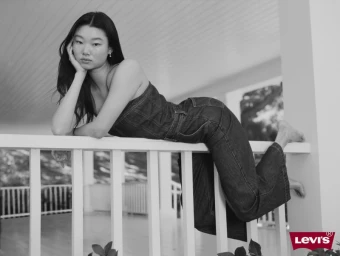 Model Yoon Young Bae wearing a denim jumpsuit reclining against a white porch railing for Levi's Spring 2025 campaign.