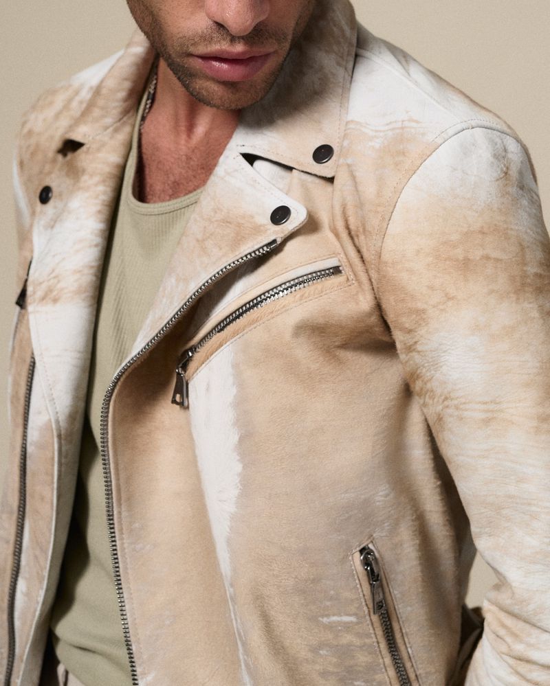 Close-up studio shot of an adult male wearing a weathered beige and white leather biker jacket and light green t-shirt.