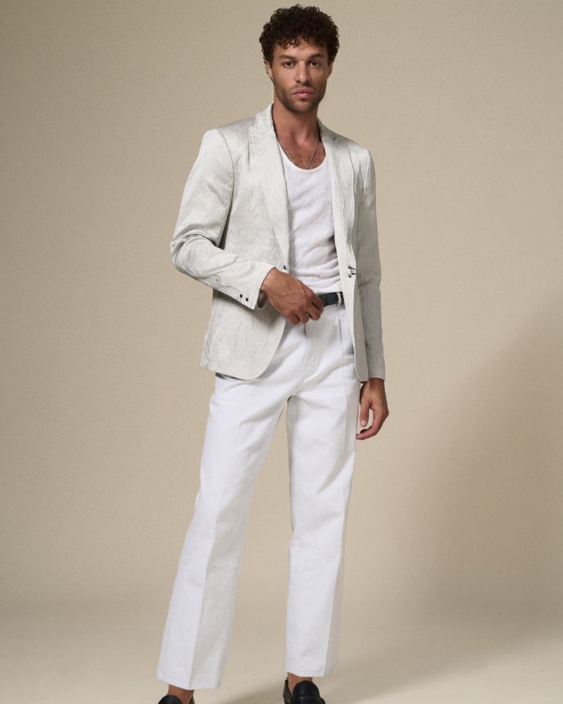 A full-length shot of a man wearing a white suit with a white shirt and black shoes, posing against a neutral background.