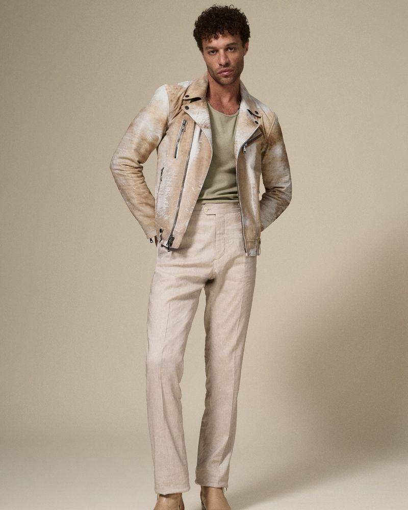 Full-length studio shot of an adult male wearing a light tan leather jacket and matching trousers, posing in front of a neutral backdrop.