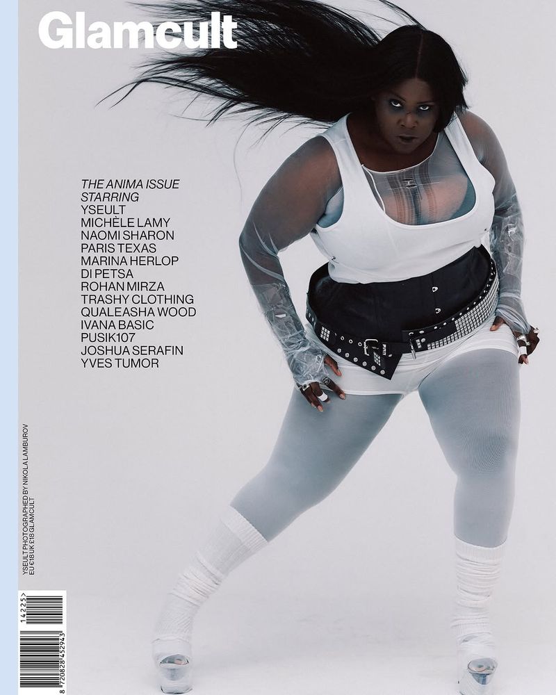 Magazine cover shot of an adult female model posing in white athleisure wear and statement studded belt against a pale blue backdrop.
