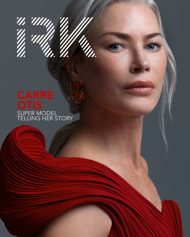 Magazine cover featuring a close-up of a supermodel with short white hair in a pleated red gown, gazing directly at the camera.