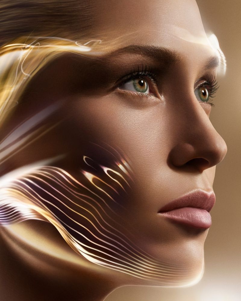 Close-up of a woman's face with light brown skin, light green eyes, pink lips, and abstract golden light patterns.