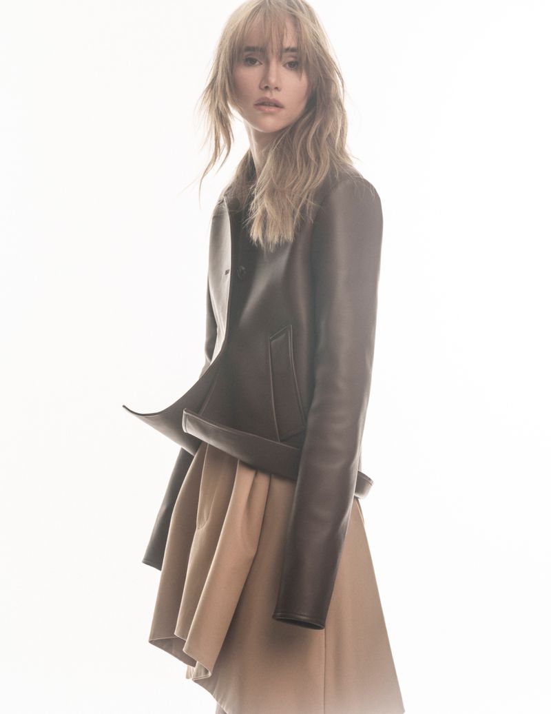 Portrait of a woman in a leather jacket and skirt, posing in a photo studio setting. Fashion editorial photography against a white background.