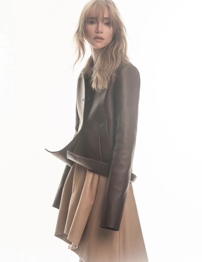 Suki Waterhouse wearing a brown leather jacket and tan skirt against a bright white background for Elle Japan.