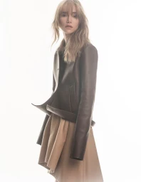 Suki Waterhouse wearing a brown leather jacket and tan skirt against a bright white background for Elle Japan.