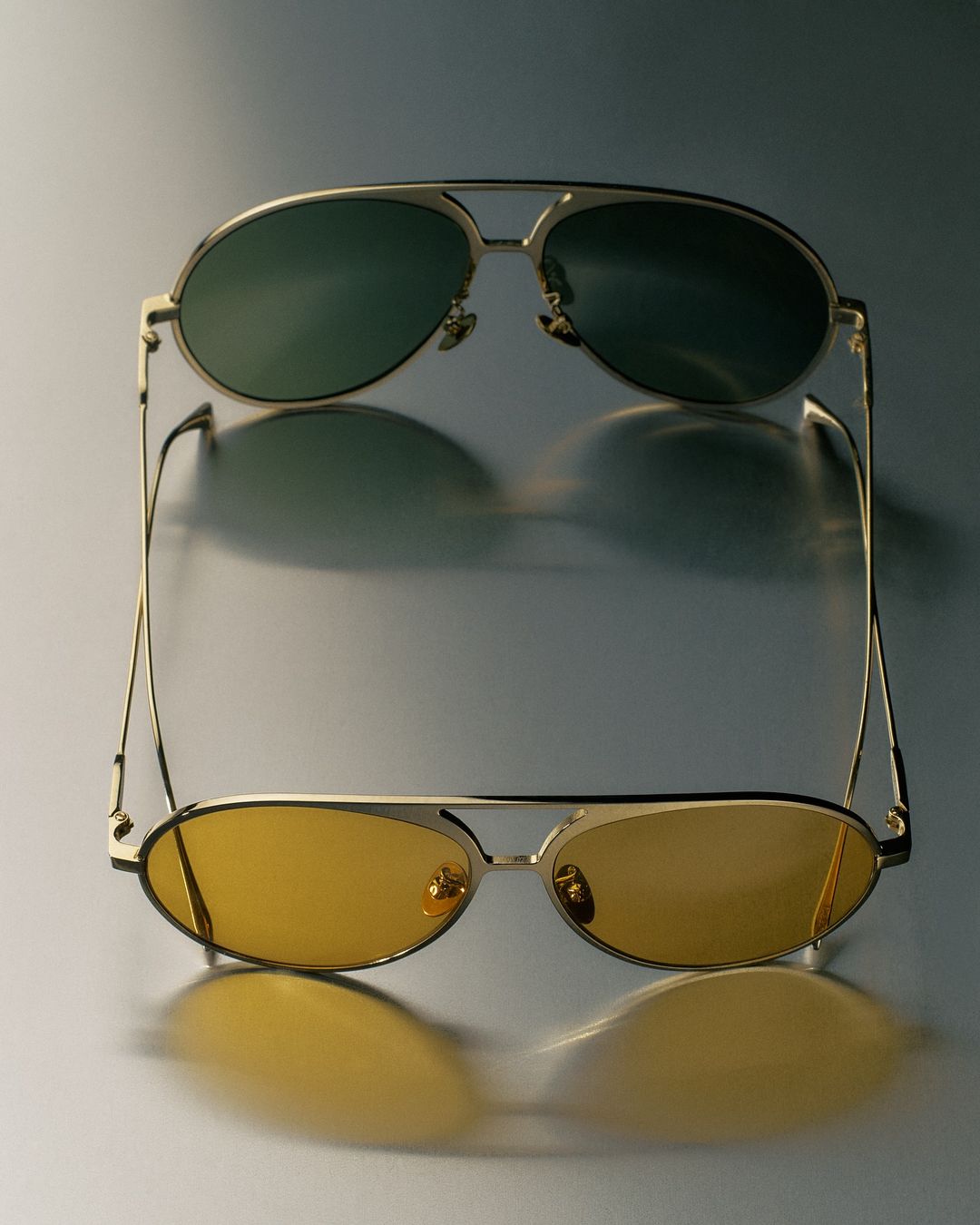Two pairs of aviator-style sunglasses are displayed, one with green lenses and the other with yellow lenses, on a gradient background.