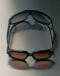 Black sunglasses with tinted lenses positioned against a reflective grey studio gradient background.