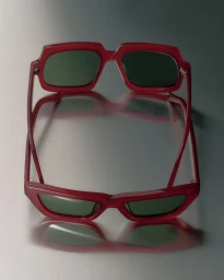 Red framed sunglasses resting on a glossy metallic reflective surface.