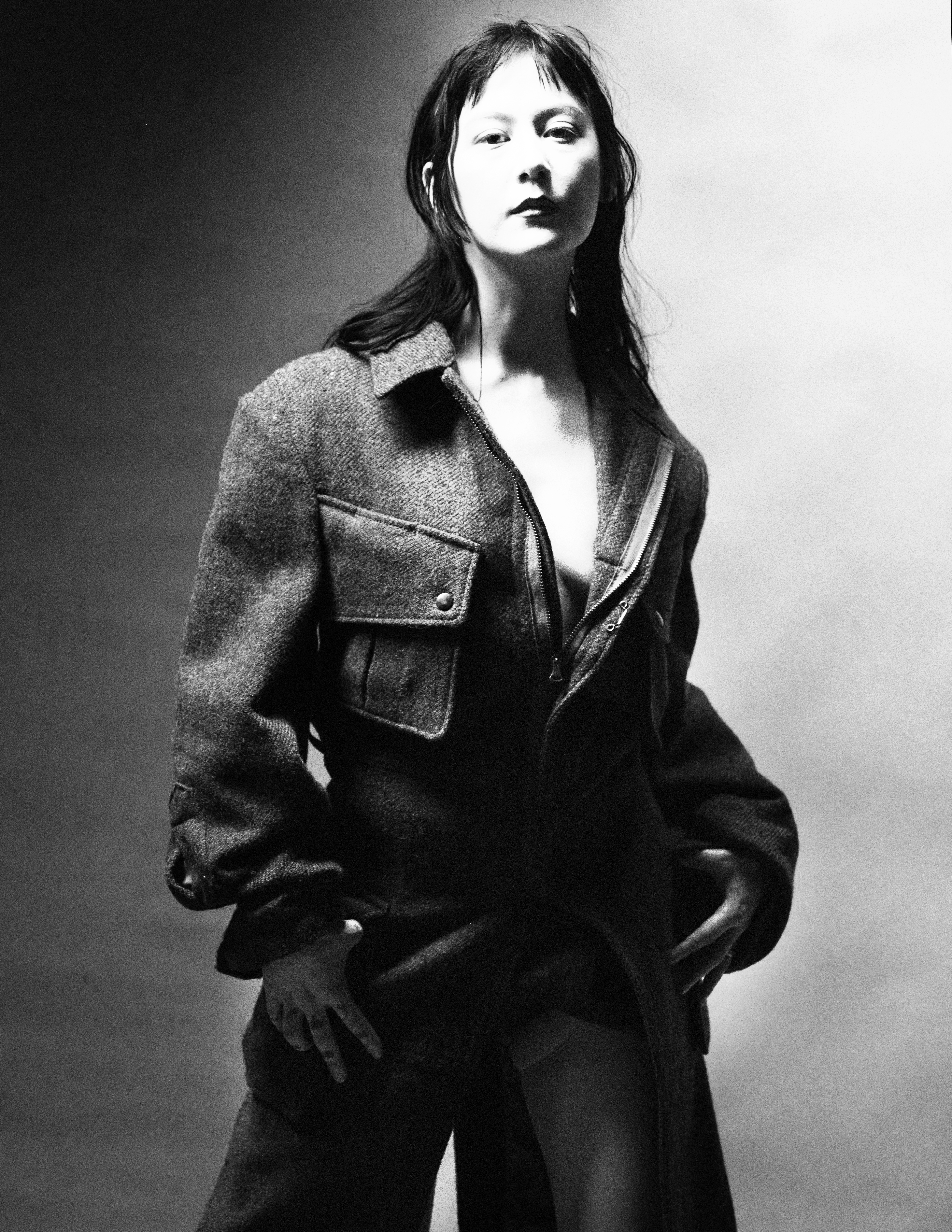 Monochrome portrait of an Asian woman in an unzipped coat, posing in a photo studio with dark hair and direct gaze, artistic shot.