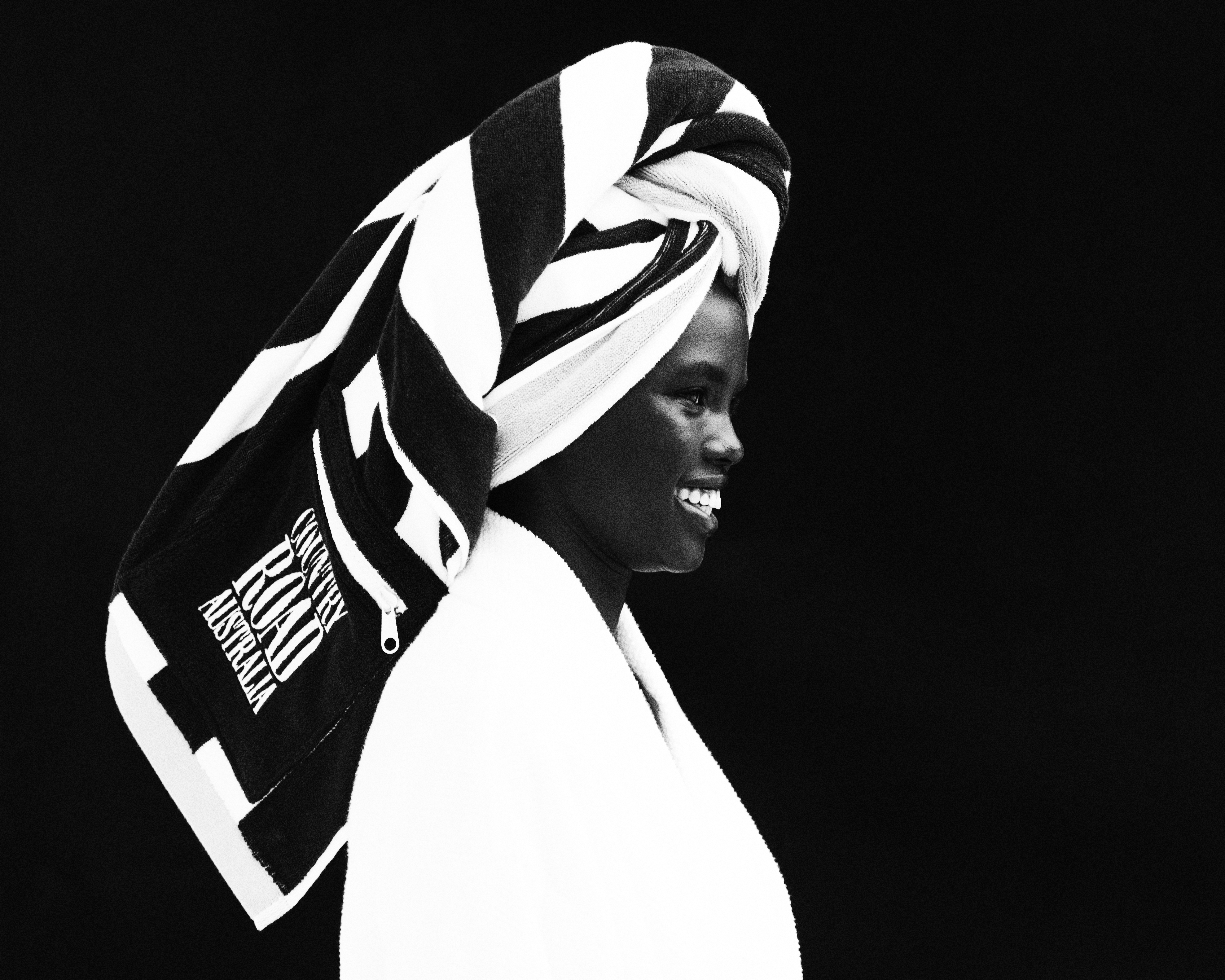 Striking black and white profile of an adult woman with a striped towel wrapped on her head, smiling with a dark background.