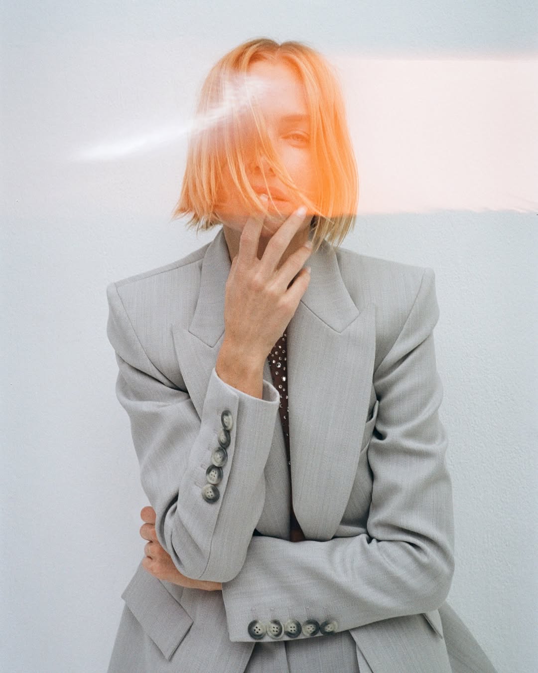 Adult female posing in grey blazer and pants. Indoor shot features a white background, studio lighting, and a contemporary fashion aesthetic.