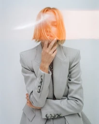 Model with orange-tinted hair covering eyes wearing a grey blazer against a white background for Alex Perry Resort 25
