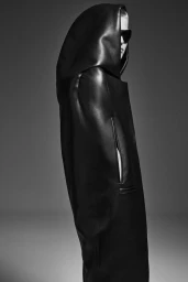 Model wearing a black hooded leather coat and dark sunglasses against a seamless grey backdrop.