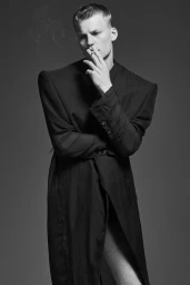 Model Timo Pan wearing a structured black coat smoking a cigarette against a grey studio backdrop for Numero Netherlands.
