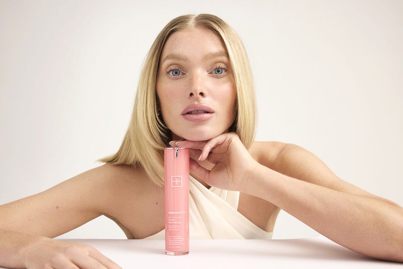 Adult female posing indoors with pink beauty product, illuminated by studio lighting against a plain background with neutral hues.