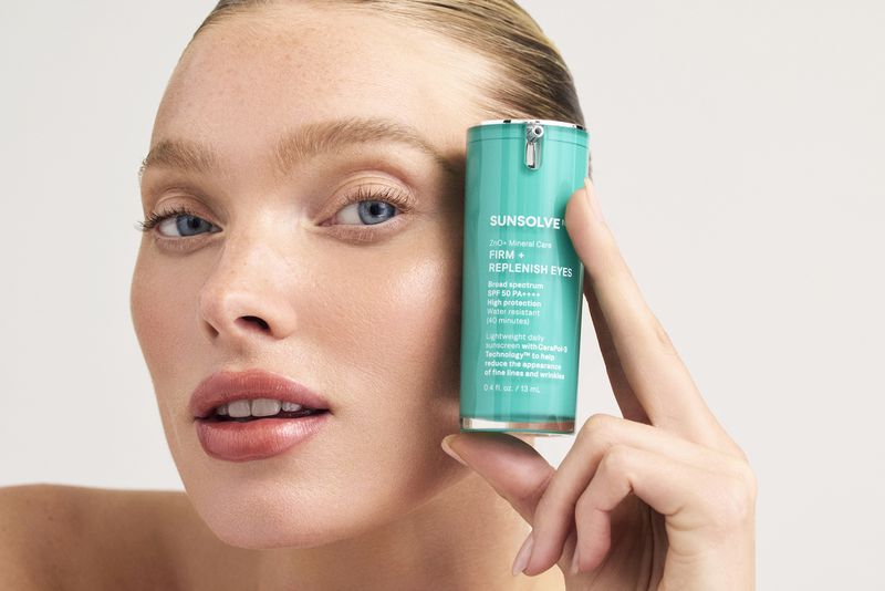 Woman holds Sunsolve skincare product for eyes. Beauty shot with close-up view. White background, medium shot focusing on the product.