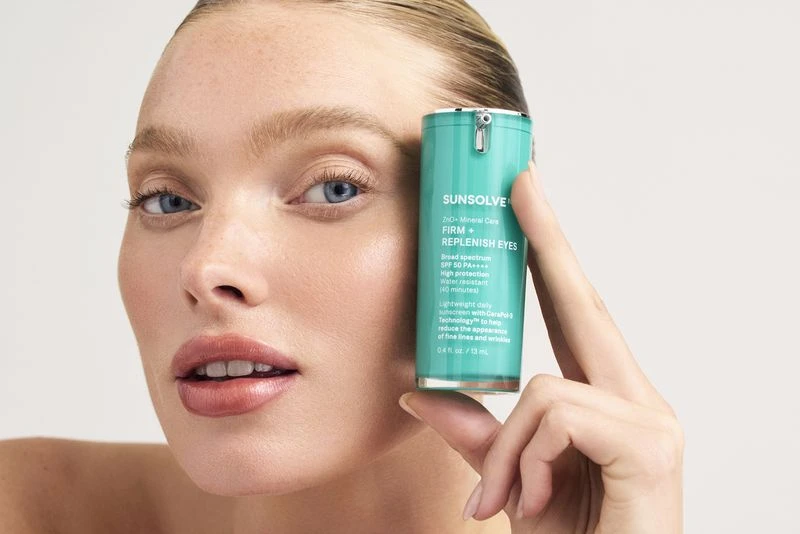 Woman holds Sunsolve skincare product for eyes. Beauty shot with close-up view. White background, medium shot focusing on the product.