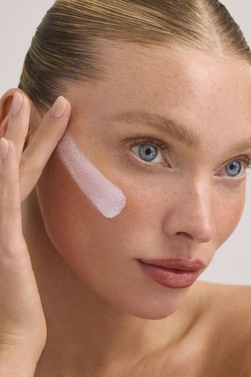 Close-up of a light-skinned woman applying face cream, highlighting beauty and skincare in a clean, bright indoor setting.