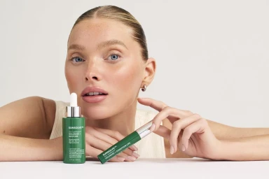 Elsa Hosk holding green SunsolveMD bottles against a white background