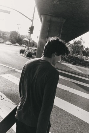 Black and white street photography featuring a young man walking across a crosswalk carrying a skateboard in an urban environment.