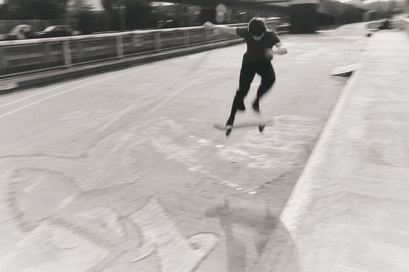 Skateboarder performing an aerial trick on a ramp in a black and white action shot in an urban environment with blurred motion.