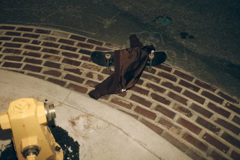 Skateboard and brown jacket laying on brick steps next to a yellow fire hydrant in an urban environment, captured at night.