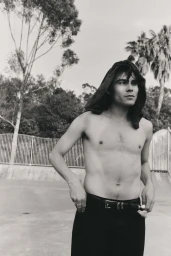 Monochrome portrait of Andrey Tarasov standing shirtless by a skate ramp with a towel on his head.
