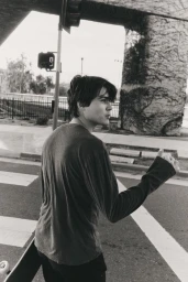 Andrey Tarasov carrying a skateboard on an asphalt street with traffic lights overhead in a black and white editorial image