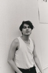 Monochrome portrait of a young man wearing a light tank top leaning against an exterior wall in Los Angeles for HERO Magazine.