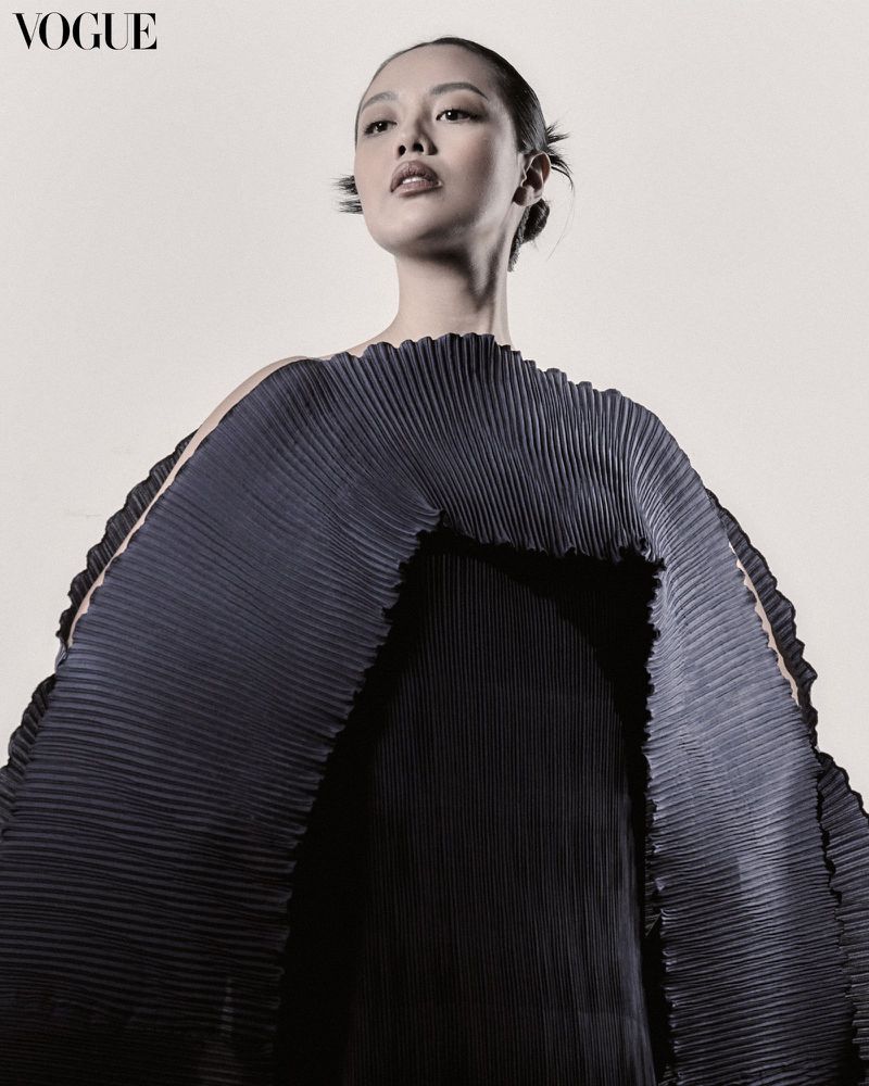 Portrait of a woman wearing a pleated dress, shot in a photo studio with white background, and natural lighting for a fashion editorial.