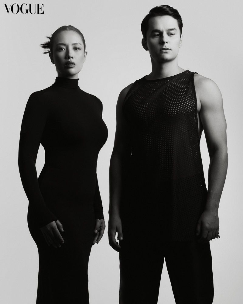 Monochrome studio shot featuring a woman in a form-fitting dress and a man in a mesh tank top, set against a light grey background.