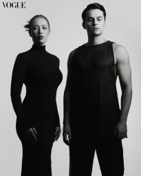 Black and white portrait of a woman in a long-sleeve black dress and a man in a patterned tank top against a plain light background