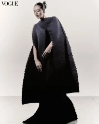 Model wearing a structured dark pleated gown posing against a plain neutral background for Vogue Philippines