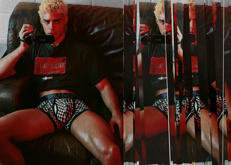 Indoor portrait of a muscular adult male in underwear, posing on a leather couch, holding a Canon camcorder. Red lighting and unique sliced effect.