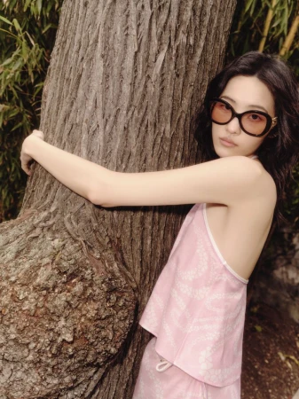 Elegant Asian woman in pink outfit and oversized glasses embraces a tree in an outdoor setting. Fashion shot with a focus on natural beauty.