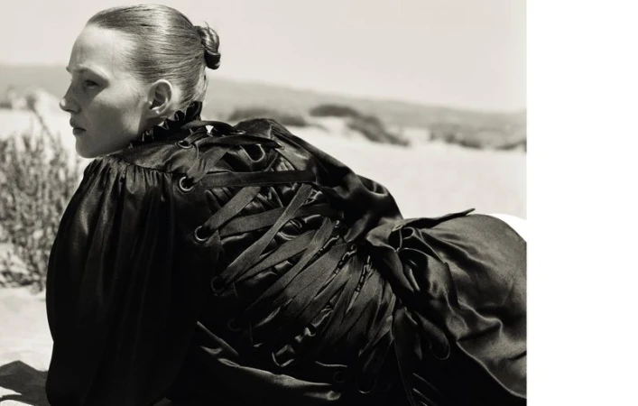 Monochrome shot of a fair-skinned woman lying down in a black dress with ribbon lacing, an outdoor setting, and high contrast lighting.