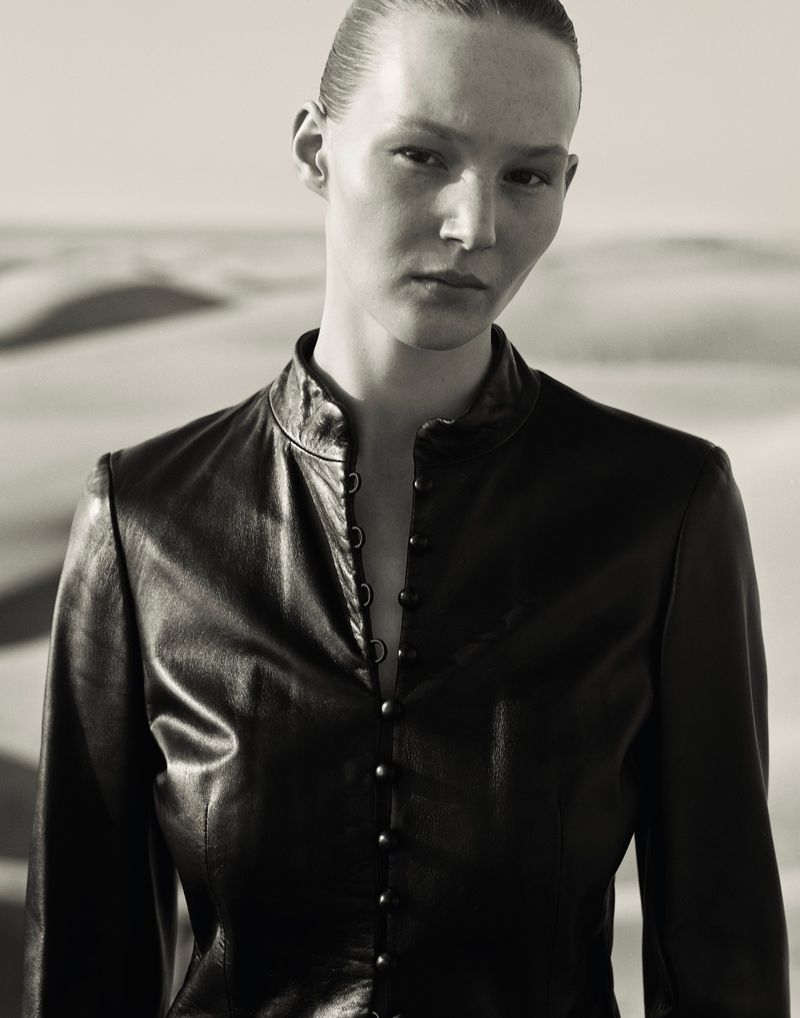 Monochrome portrait of a woman in a black leather jacket against a desert backdrop, showcasing fashion and natural beauty.