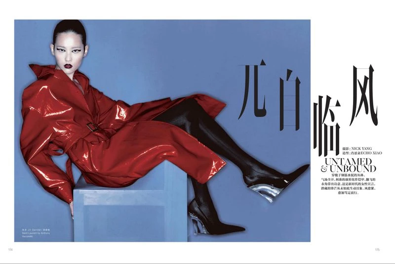 Editorial fashion shot of Asian female model in a red patent leather trench coat, black hosiery, and black heels, posing in studio.
