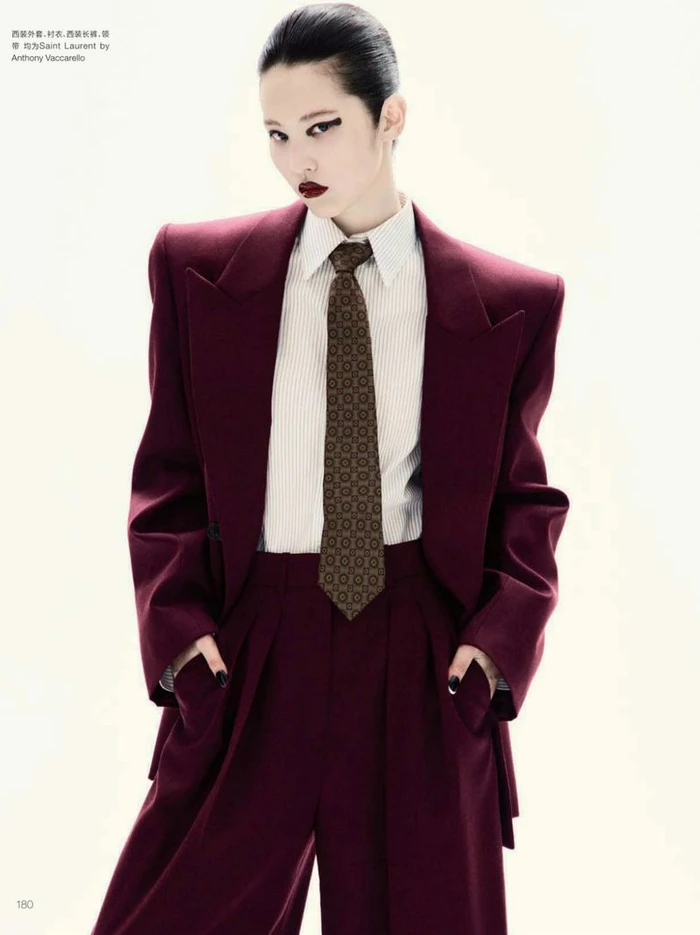 Model in burgundy suit jacket and trousers with pinstripe shirt and patterned tie against white seamless backdrop
