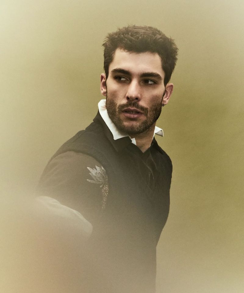 Portrait of a handsome adult man with dark hair looking over his shoulder wearing a black shirt and white collared shirt. Outdoor environment.