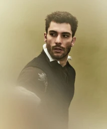 Portrait of male model Paolo Busti wearing a dark vest over a white collared shirt against a muted gradient background.