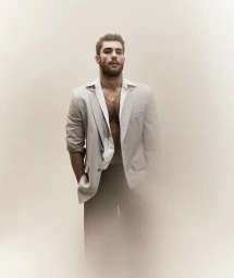 Model Paolo Busti in an unbuttoned white shirt and grey blazer against a neutral backdrop for Le Mile Magazine.