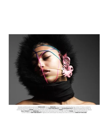 Close-up fashion portrait of an African-American woman with colorful string details and statement earrings against a grey backdrop.
