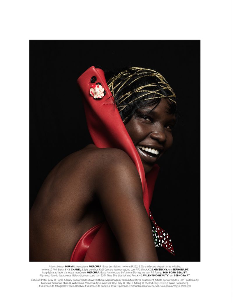 Portrait of a smiling Black woman with dark skin and a red, sculptural fashion piece, accessorized with a gold head wrap against a black background.
