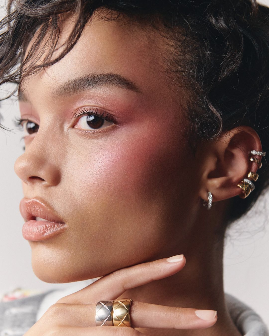 Close-up beauty portrait of Whitney Peak wearing quilted gold and silver rings and multiple ear cuffs against a light background